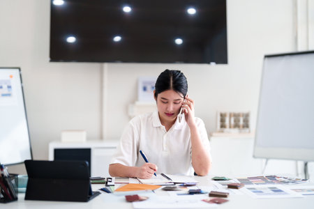 Interior designer making business call while working on color and material selection at design studio deskの写真素材
