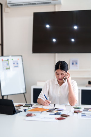 Interior designer making business call while working on color and material selection at design studio deskの写真素材