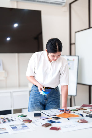 Young architect selecting materials and color swatches while standing at modern interior design workstationの写真素材