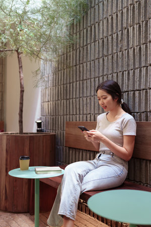 Woman enjoying peaceful coffee break while browsing smartphone at cozy outdoor cafe tableの写真素材