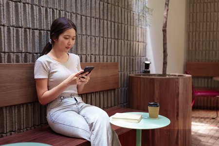 Woman enjoying peaceful coffee break while browsing smartphone at cozy outdoor cafe tableの写真素材