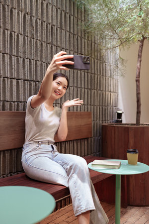 Young woman taking a cheerful selfie during relaxing time at outdoor cafe with cozy natural atmosphereの写真素材