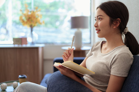 Calm young woman sitting on couch and writing in her diary during a peaceful moment in cozy home settingの写真素材
