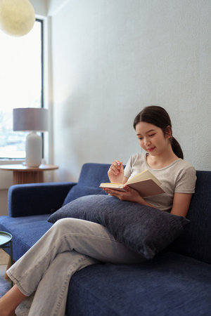 Calm young woman sitting on couch and writing in her diary during a peaceful moment in cozy home settingの写真素材