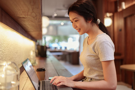 Young woman using laptop and browsing internet at modern cafe counter during casual solo work sessionの写真素材