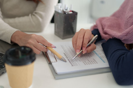 Close-up image of adult Asian women discussing investment plans using a calculator. Focus on financial documents, pens. Ideal for illustrating Muslim business finance.の写真素材
