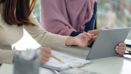 Two adult Asian women, one wearing a hijab, are collaborating on a Muslim business strategy using a tablet. They are analyzing financial data and planning investment.の写真素材