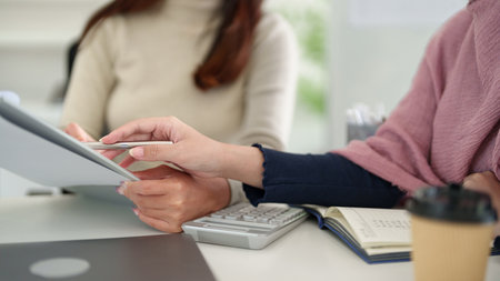 Adult Asian women in Muslim business meeting collaborate, review finance documents, and plan for success at the office desk. Focus on teamwork, paperwork, and accounting strategy.の写真素材