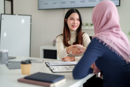 Successful Muslim business collaboration. An Asian women shaking hands with Muslim businesswoman at office. Partnership deal with financial growth.の写真素材