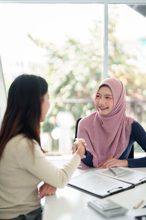 A young Asian Muslim businesswoman wearing a hijab shakes hands with her partner during a business meeting. Focus on Muslim finance, deal agreement, and startup success.の写真素材