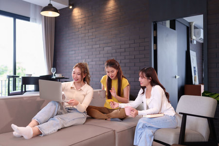 Three young Asian women are relaxing at home and shopping online with a laptop using a credit card The concept represents friendship lifestyle technology and e commerce and relaxationの写真素材