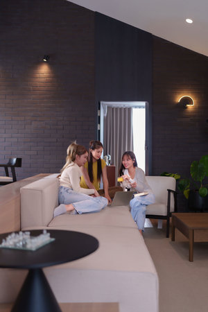 Three Asian women, young adults, are sitting on a sofa. One is holding a credit card, looking happy. Home decor is modern.の写真素材