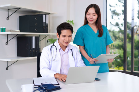 Asian adult doctor and nurse collaborate in a modern clinic using a laptop to review patient records. They provide healthcare solutions with medical expertise and teamwork.の写真素材