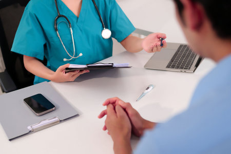 Adult Asian women doctor in teal scrubs with stethoscope consulting and discussing a medical record with patient in clinic office with laptop and thermometer. Healthcare professional.の写真素材