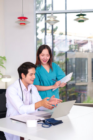 Asian doctor and nurse discussing patient care on laptop in a modern clinic office. Medical team collaboration for patient health. Healthcare professional in the workplaceの写真素材