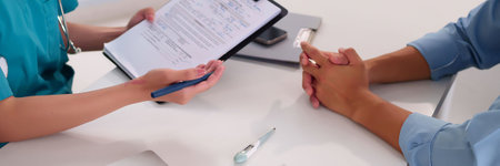 Doctor meeting with patient for consultation in office. Healthcare professional examining patient and discussing treatment options. Doctor holds a medical chart, and thermometer on the table.の写真素材