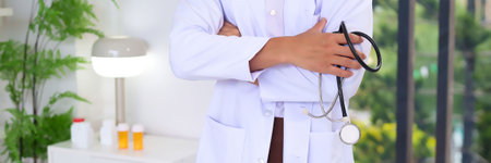 Close up of an adult Asian doctor in white coat with stethoscope arms crossed in hospital. Professional medical personnel for diagnosis promoting wellness healthcare.の写真素材