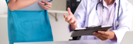 A scene showing Asian adult doctor with a stethoscope and a coworker reviewing paperwork. This captures patient consultation, diagnosis, healthcare checkup in clinic settings.の写真素材