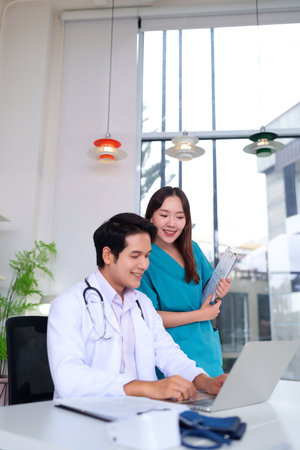 An Asian adult doctor and nurse teamwork at clinic. They are working on a laptop for medical report and analyzing health care. Professional hospital staff for patient care.の写真素材