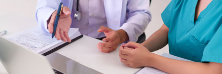 Asian doctor explaining treatment details to patient during consultation at clinic office. Hospital healthcare professional provides explanation of medical information to adult patient.の写真素材