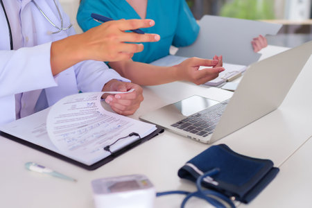 Adult medical professionals wearing scrubs reviewing patient medical history on a laptop analyzing test results discussing treatment options and making informed decisions to improve health.の写真素材
