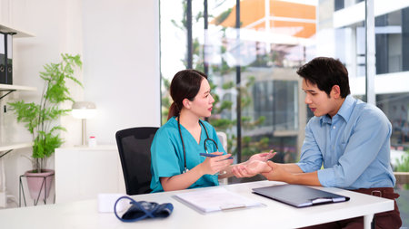 An Asian doctor checks the young Asian male patient's wrist for pain, offering consultation and medical care during a clinic visit providing health checkup diagnosis and treatmentの写真素材