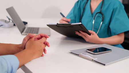 Adult Asian women doctor in green scrubs taking notes on a patient chart during consultation for medical treatment healthcare and wellness advice in a clinic or hospitalの写真素材