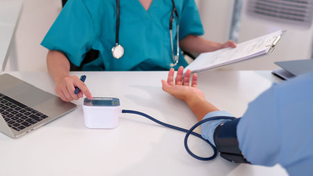 Adult Asian women doctor checking blood pressure of patient using electronic equipment stethoscope and document on white table healthcare medical conceptの写真素材