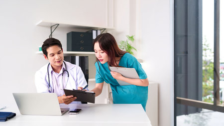 Asian adult doctor and nurse collaborating on a patient's treatment plan in clinic setting. They are discussing documents. Medical teamwork for better healthcare services in hospital setting.の写真素材