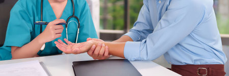 Asian woman doctor examines adult Asian man's wrist for pain or discomfort in a clinic setting, showing healthcare medical professional consultation for diagnosis.の写真素材