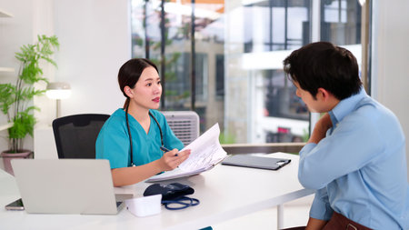 Asian women doctor in scrubs explains health report to young Asian men patient at clinic. Doctor consults about diagnosis treatment and wellness healthcare for advice.の写真素材