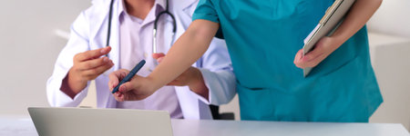 Adult Asian doctors and nurse working together in clinic. Hands are writing notes on laptop during a discussion about patient treatment and healthcare. Focus on teamwork and collaboration.の写真素材