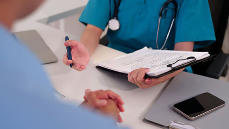 Asian adult woman doctor in clinic office explaining diagnosis to patient with clipboard giving healthcare advice using pen during consultation for medical treatmentの写真素材