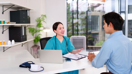 Young Asian women doctor in scrubs consulting with an adult male patient in a clinic office. They are discussing the diagnosis and treatment plan in an exam room Healthcare professional in officeの写真素材