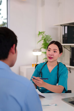 Asian adult woman doctor in green scrubs explaining medical information to a patient in clinic. She is holding a pen and discussing diagnosis treatment and preventative care.の写真素材