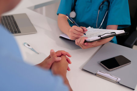 Asian women doctor in blue uniform writes medical history on clipboard. Hands of patient. Medical concept with stethoscope, thermometer and smartphone on deskの写真素材