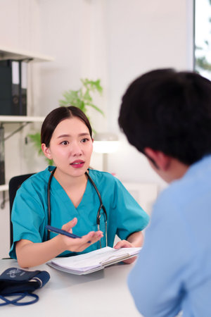 An adult Asian women doctor in green scrubs explains medical report to patient during clinic consultation offering advice about healthcare treatment discussion and checkup for recovery.の写真素材