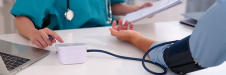 Asian doctor measuring blood pressure of older patient for health monitoring and medical exam using electronic sphygmomanometer device in clinic for patient wellness assessment.の写真素材