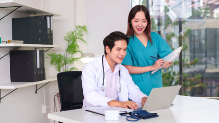 Young Asian doctor and nurse are collaborating on a laptop and discussing patient care in a hospital office. This image captures the essence of healthcare teamwork, medical professionalism and patient treatmentの写真素材