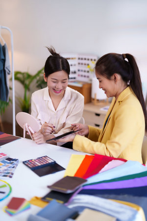 Two Asian adult women are consulting on personal color matching to choose the right color tone and makeup for fashion with color swatches at the studio.の写真素材