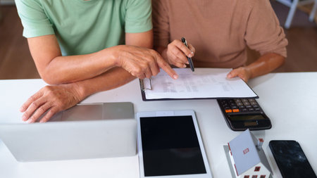 Older couple reviewing financial documents in their house. They are planning for retirement savings and home investments together. They are using technology to help.の写真素材