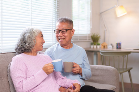 An older Asian couple enjoys coffee on the sofa in their home They share a loving moment Retirement and relaxation at home A content elder couple.の写真素材