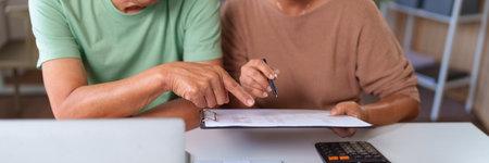 Older Asian couple going through paperwork with pen and calculator focusing on financial matters family budget or planning finances for retirement at home.の写真素材