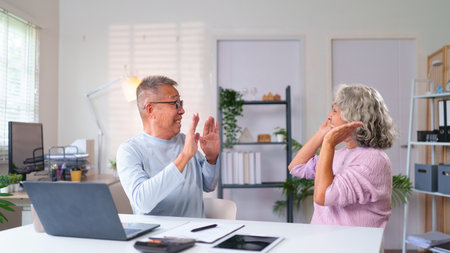 Cheerful older Asian couple having a happy time at home. They are using a laptop to video call family or friends. Modern seniors connectedness and togethernessの写真素材
