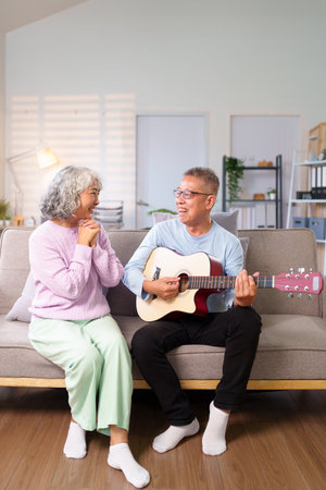 This sweet older Asian couple cherishes quality time at home as the man plays guitar for his wife They share happy and romantic moments together in their retirement.の写真素材