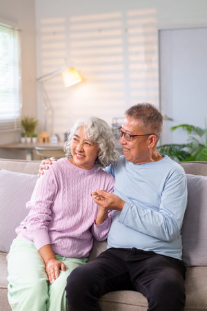 This image shows an older Asian couple, sharing a loving moment in their cozy home, perfect for...