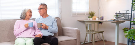 This image features a delightful older Asian couple at home. They are enjoying tea on the couch together and sharing happy moments. Capture the essence of love.の写真素材