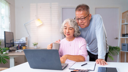 An Asian older couple is enjoying their retirement life at home, using a laptop together, and having coffee time at their home while looking at the computer screenの写真素材
