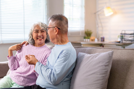 An older Asian couple shares a loving moment at home, showcasing companionship. They are living a comfortable life in their golden years filled with smiles and relaxation.の写真素材
