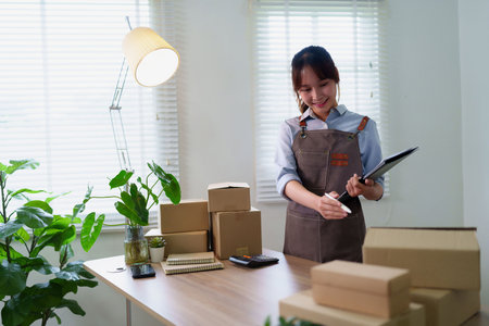 Young Asian women are working at home checking stock for delivery to customers. Small business owner with parcel box for online store or ecommerce business.の写真素材